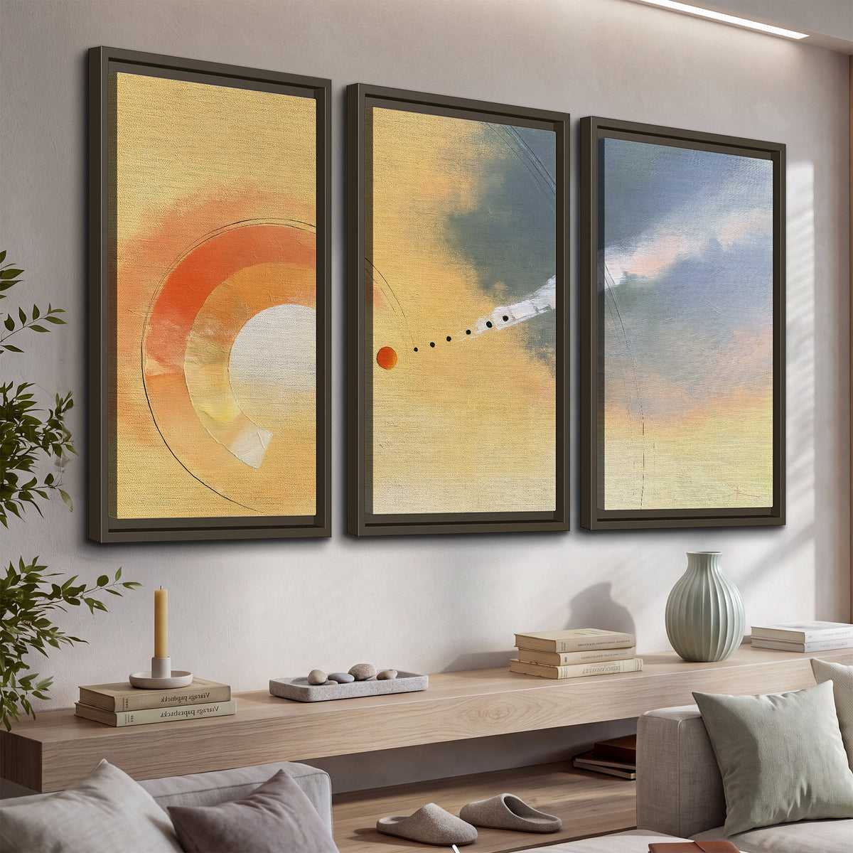A warm orange circular form and diagonal pale streaks across a muted yellow and blue field 3 piece framed canvas wall art displayed in a console