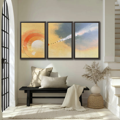 A warm orange circular form and diagonal pale streaks across a muted yellow and blue field 3 piece framed canvas wall art displayed in a entryway