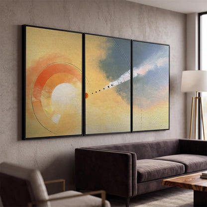 A warm orange circular form and diagonal pale streaks across a muted yellow and blue field 3 piece framed canvas wall art displayed in a modern living room