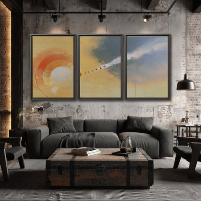 A warm orange circular form and diagonal pale streaks across a muted yellow and blue field 3 piece framed canvas wall art displayed in a industrial room