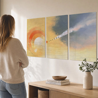 A warm orange circular form and diagonal pale streaks across a muted yellow and blue field set of 3 poster prints three panel arrangement on a wall