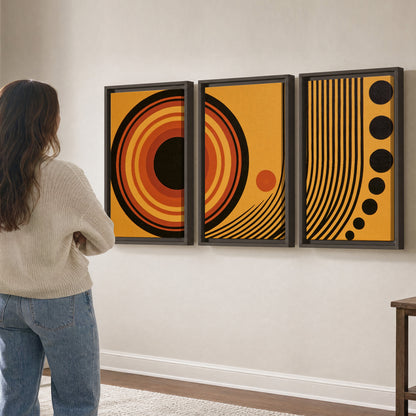 Bold black, orange and golden circles with parallel curved lines and small dots 3 piece framed canvas wall art three panel arrangement on a wall