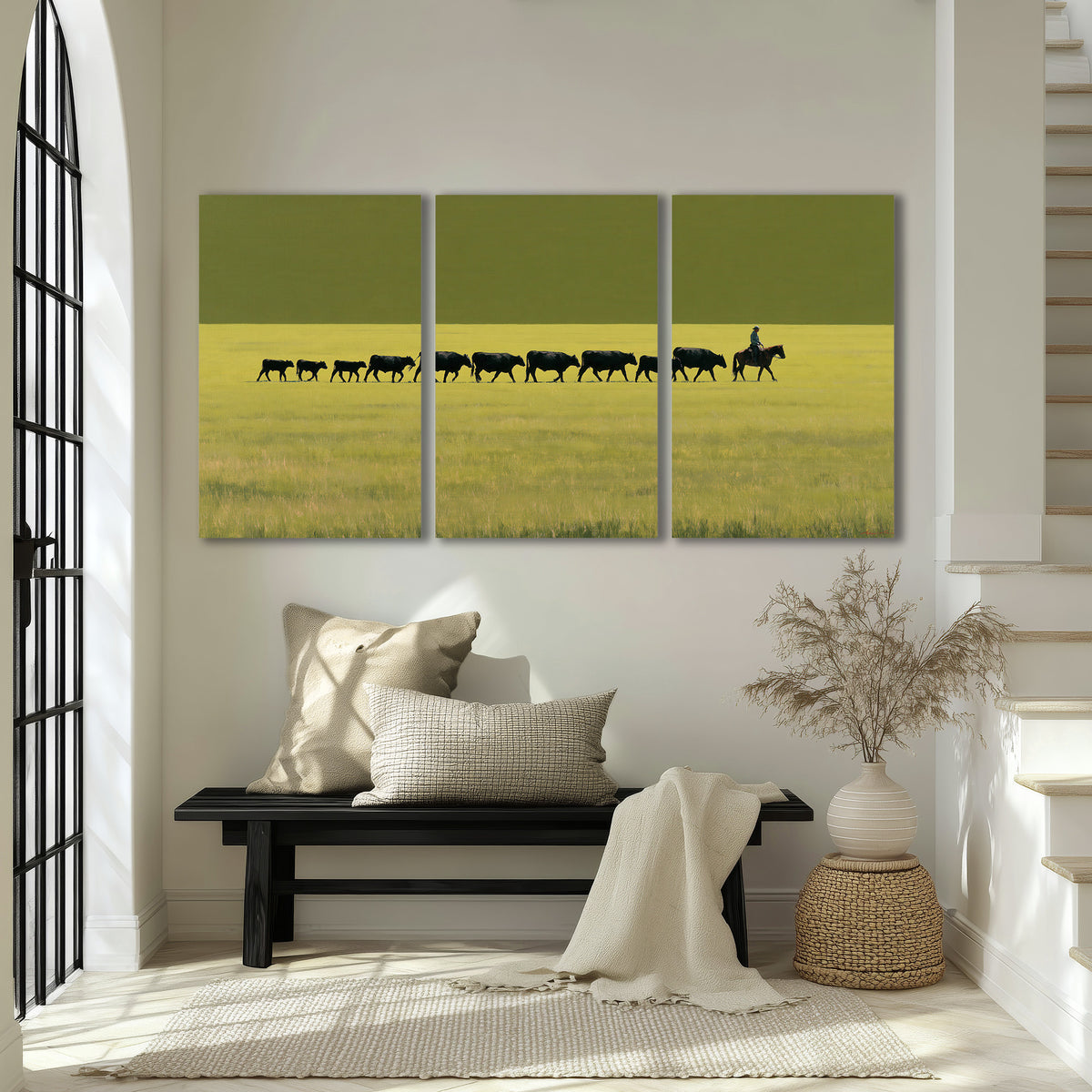 A rider leading a long line of cattle across a wide green and golden plain 3 piece canvas wall art displayed in a entryway