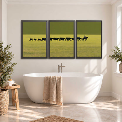 A rider leading a long line of cattle across a wide green and golden plain 3 piece framed canvas wall art styled in an interior