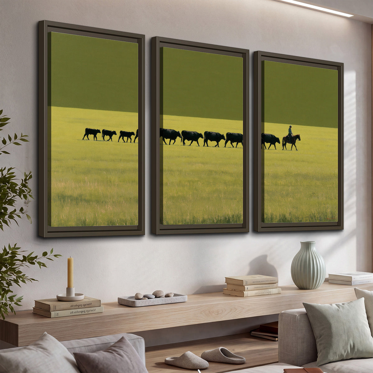 A rider leading a long line of cattle across a wide green and golden plain 3 piece framed canvas wall art displayed in a console