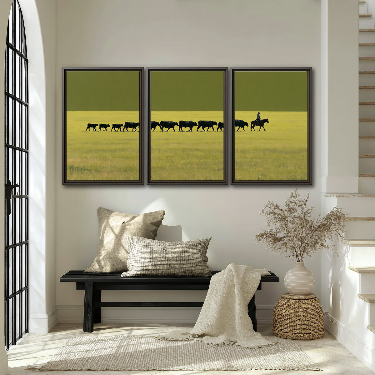 A rider leading a long line of cattle across a wide green and golden plain 3 piece framed canvas wall art displayed in a entryway