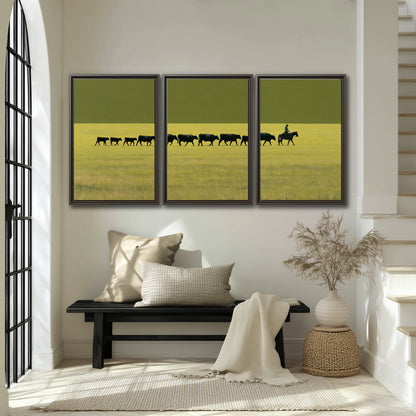 A rider leading a long line of cattle across a wide green and golden plain 3 piece framed canvas wall art displayed in a entryway