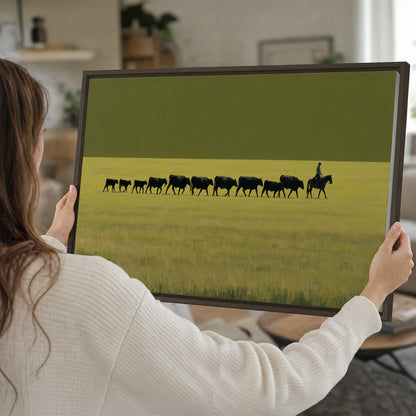 A rider leading a long line of cattle across a wide green and golden plain single framed canvas wall art held in hands