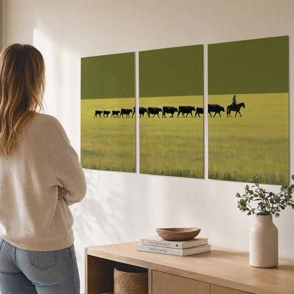 A rider leading a long line of cattle across a wide green and golden plain set of 3 poster prints three panel arrangement on a wall