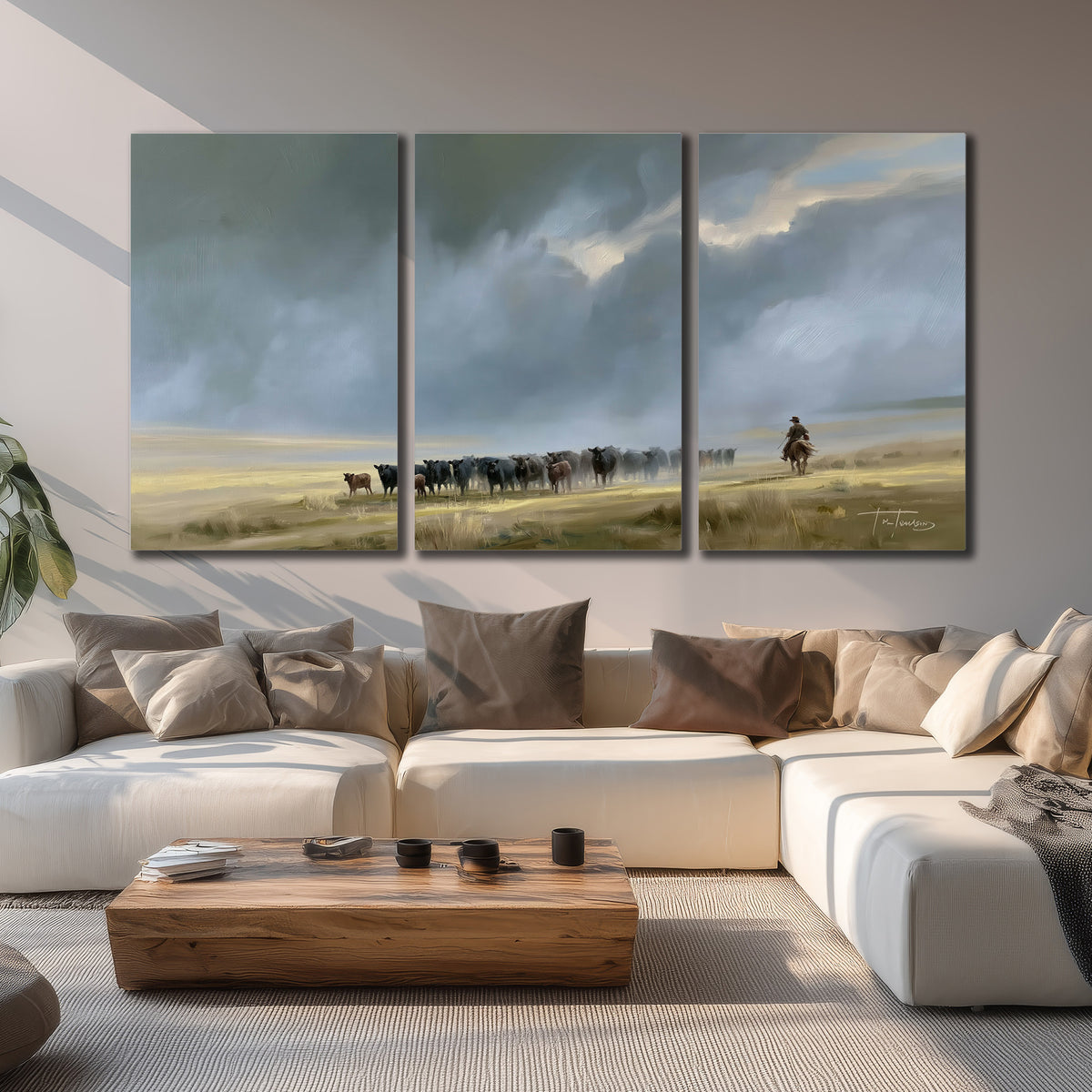 A rider and cattle moving across a sunlit grassland beneath a dramatic blue-gray sky 3 piece canvas wall art displayed in a living room