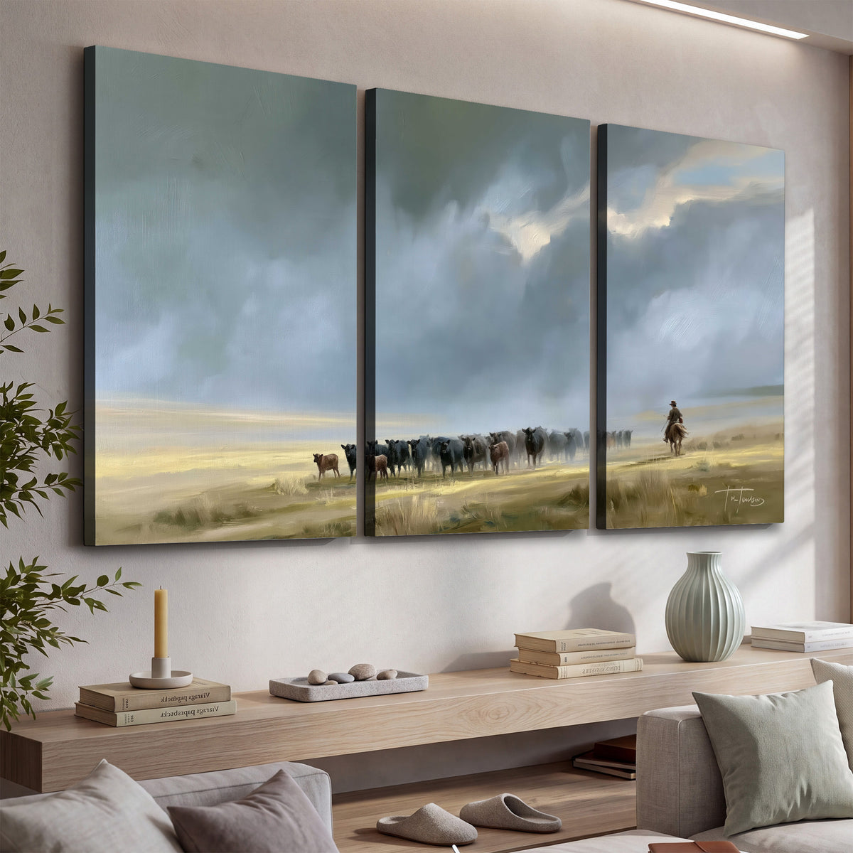 A rider and cattle moving across a sunlit grassland beneath a dramatic blue-gray sky 3 piece canvas wall art displayed in a console
