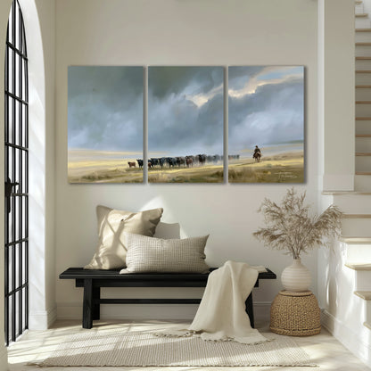 A rider and cattle moving across a sunlit grassland beneath a dramatic blue-gray sky 3 piece canvas wall art displayed in a entryway
