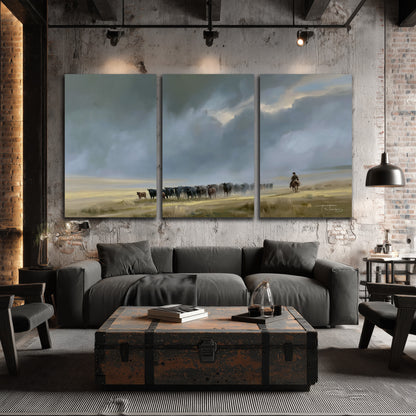 A rider and cattle moving across a sunlit grassland beneath a dramatic blue-gray sky 3 piece canvas wall art displayed in a industrial room