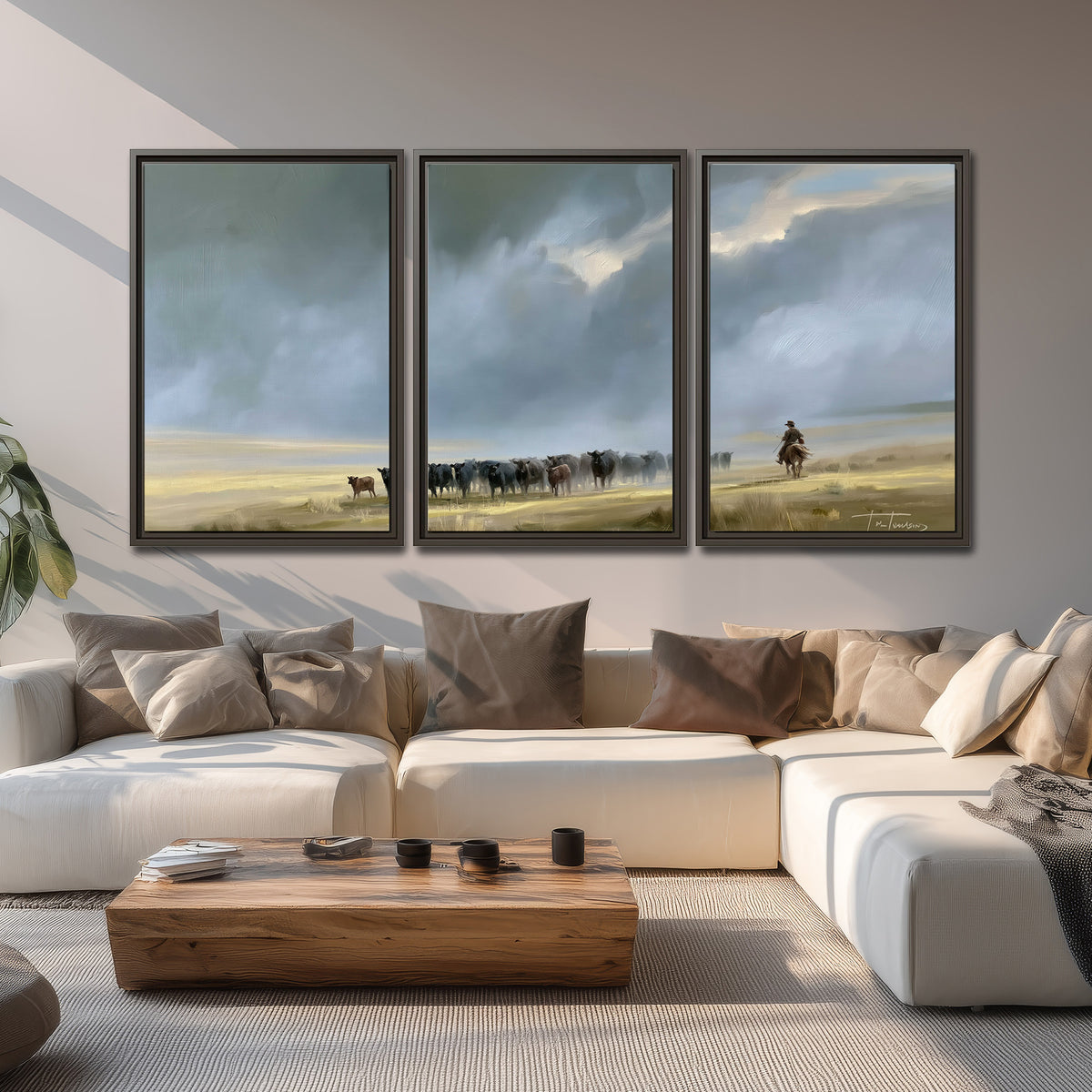 A rider and cattle moving across a sunlit grassland beneath a dramatic blue-gray sky 3 piece framed canvas wall art displayed in a living room