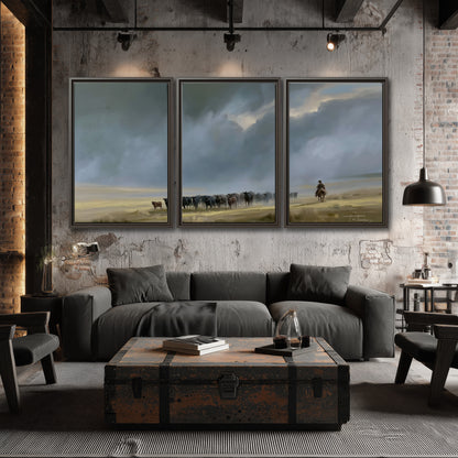 A rider and cattle moving across a sunlit grassland beneath a dramatic blue-gray sky 3 piece framed canvas wall art displayed in a industrial room