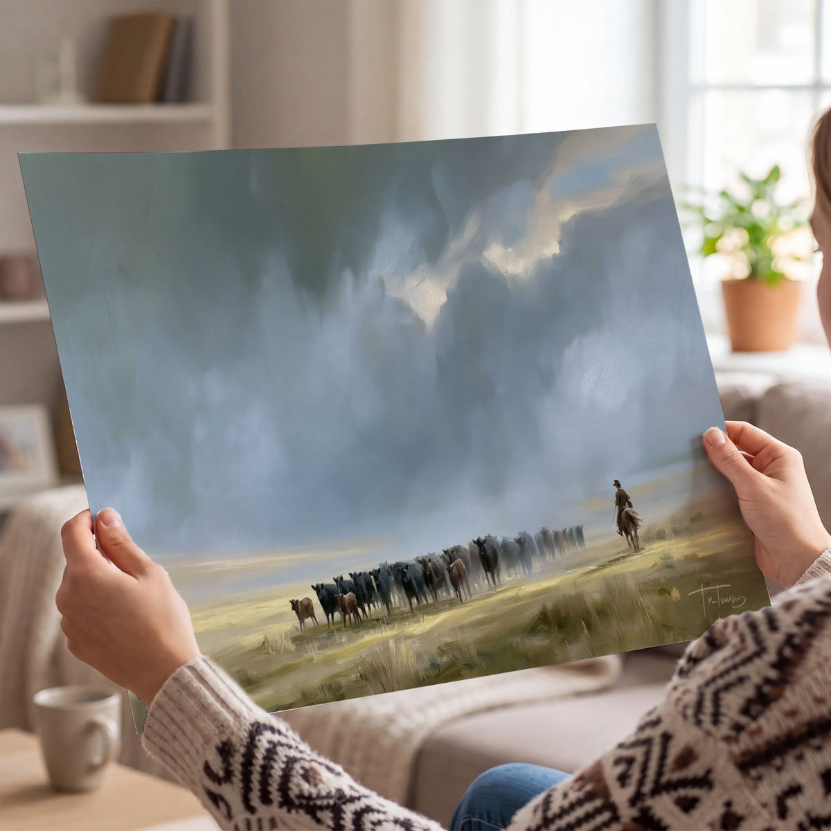 A rider and cattle moving across a sunlit grassland beneath a dramatic blue-gray sky single poster print held in hands