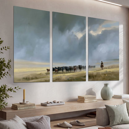 A rider and cattle moving across a sunlit grassland beneath a dramatic blue-gray sky set of 3 poster prints displayed in a console