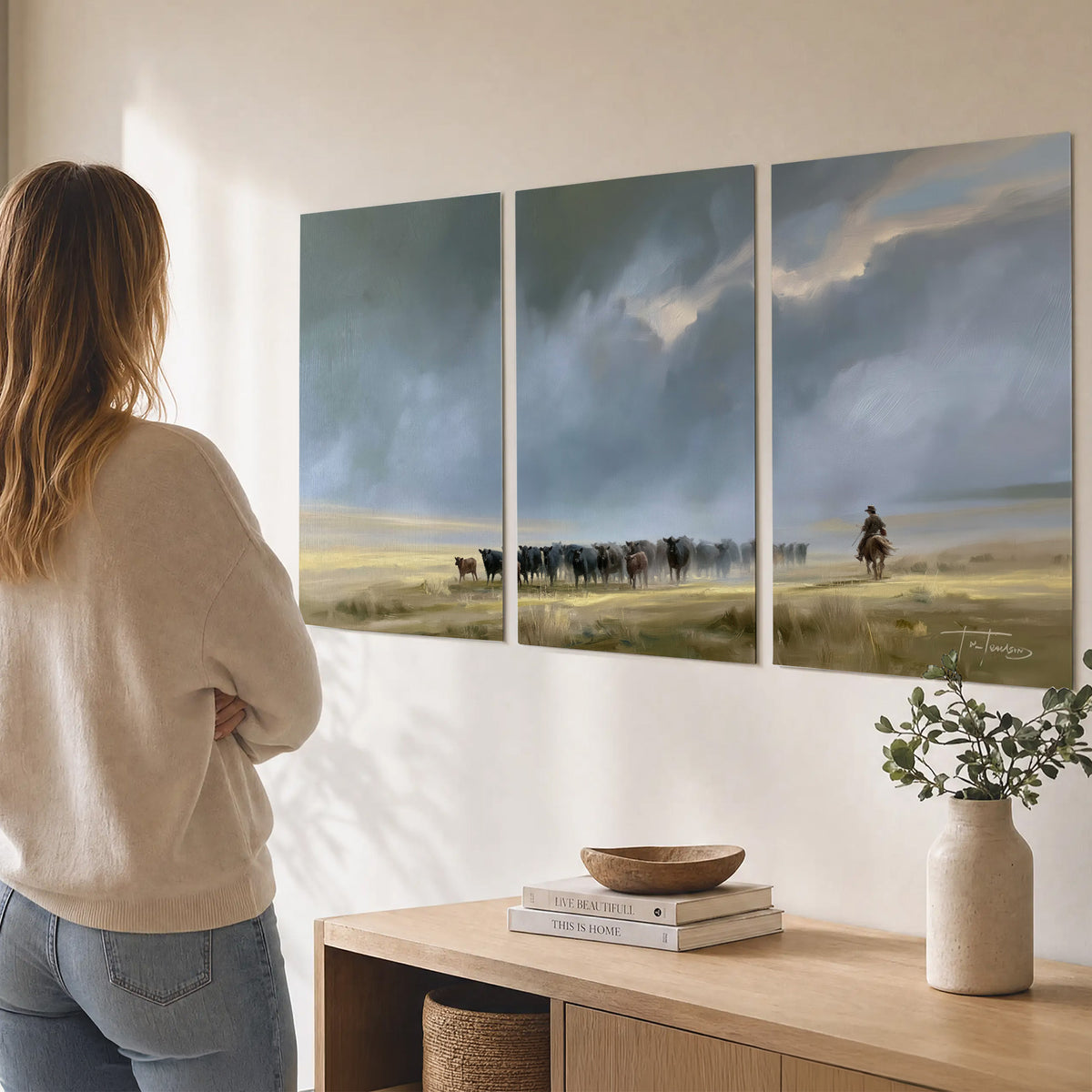A rider and cattle moving across a sunlit grassland beneath a dramatic blue-gray sky set of 3 poster prints three panel arrangement on a wall